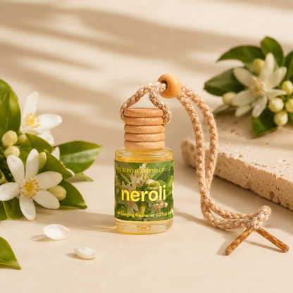Neroli hanging car freshener bottle with wooden cap and braided cord among white blossoms and green leaves